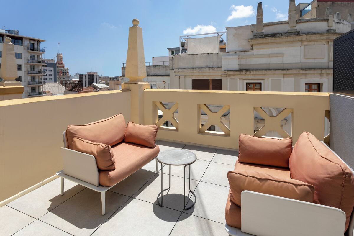 A rooftop terrace with two sofas and a small round table, offering a view of the cityscape.