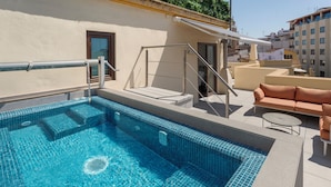 Una piscina en la azotea con barandilla de vidrio, un sofá y una mesita.