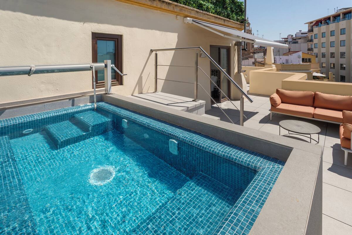 A rooftop swimming pool with a glass railing, a sofa, and a small table.