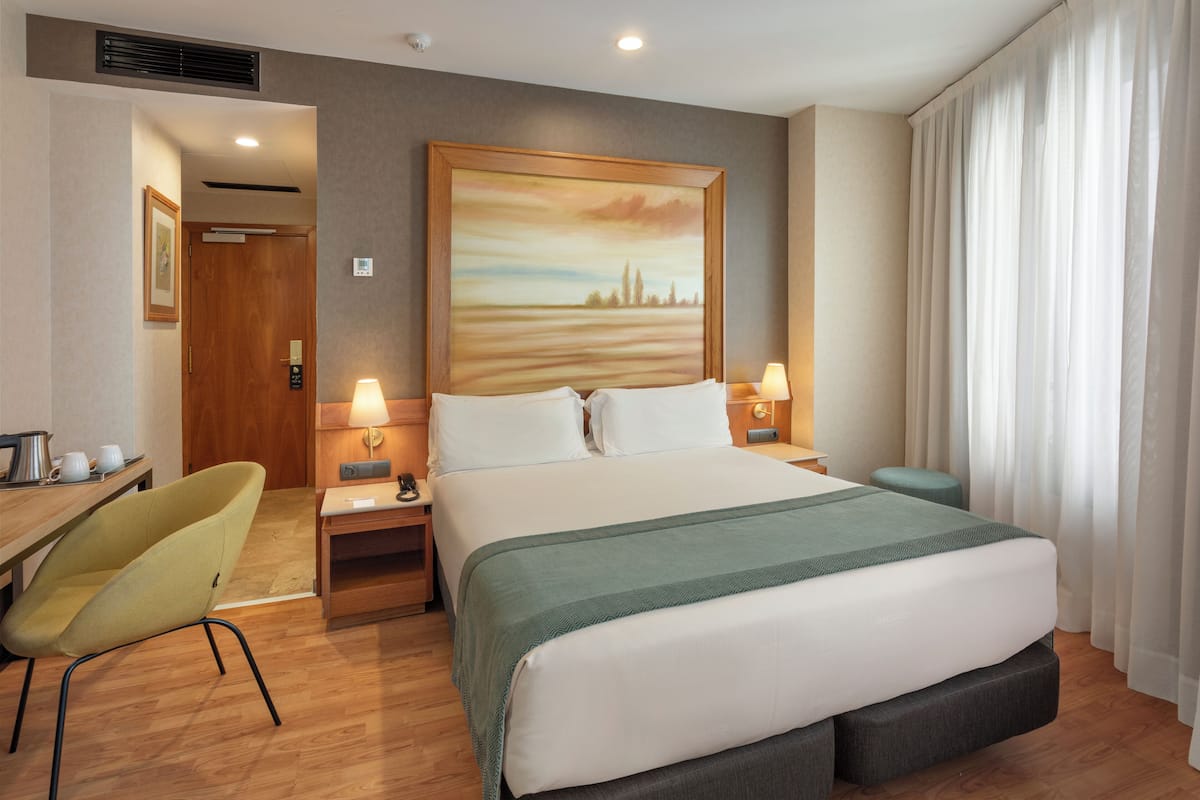 A hotel room with a large bed, two bedside tables with lamps, a chair, and a painting on the wall.