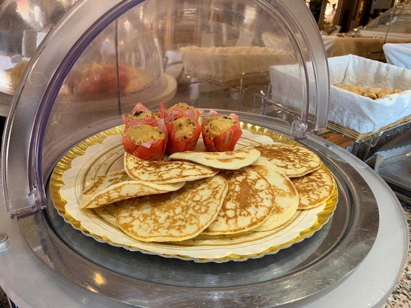 Een ontbijtbuffet met pannenkoeken en muffins onder een glazen koepel.