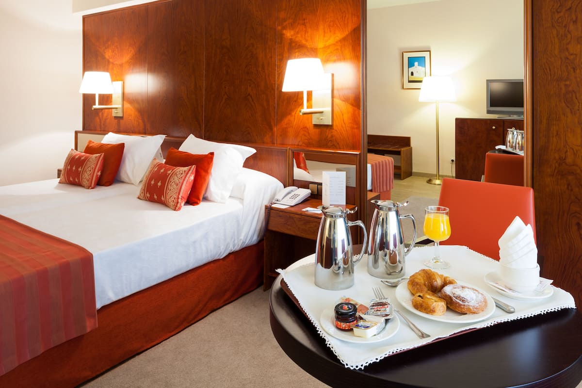 Een hotelkamer met een bed, nachtkastje en een ontbijtbakje met gebak, koffie en sap.