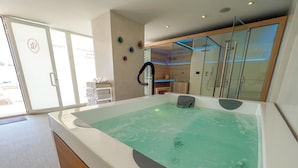 Un spa moderno con un amplio jacuzzi, puertas de cristal que dan a un espacio exterior y un banco de madera.