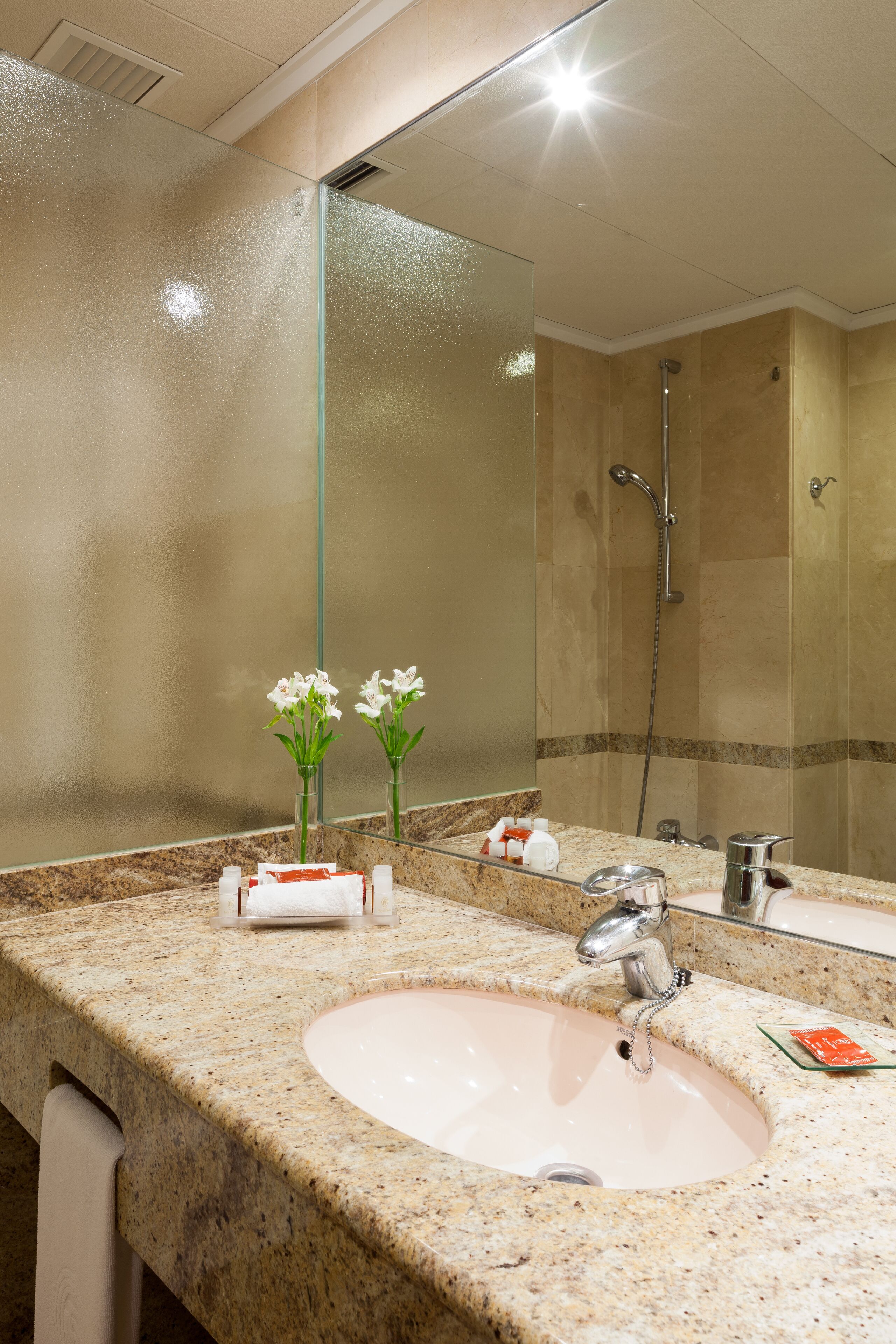 A bathroom with a granite countertop, a sink, a mirror, and a shower.