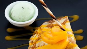 A dessert plate with a crepe topped with caramelized fruit and a small bowl of green ice cream.