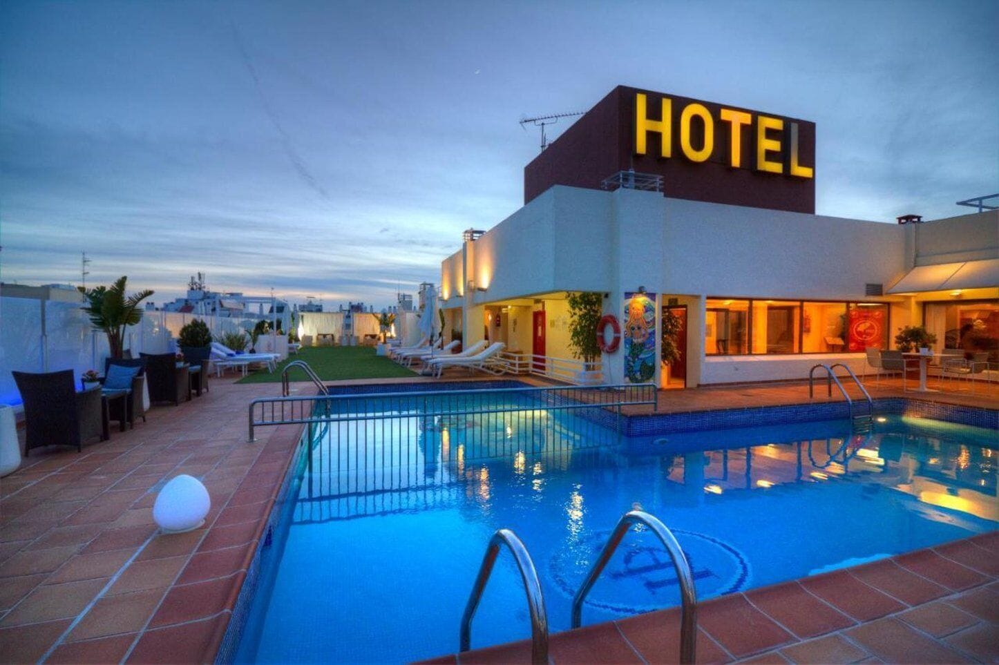 A hotel with a swimming pool, lounge chairs, and a view of the cityscape.