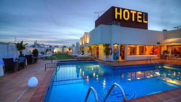 A hotel with a swimming pool, lounge chairs, and a view of the cityscape.