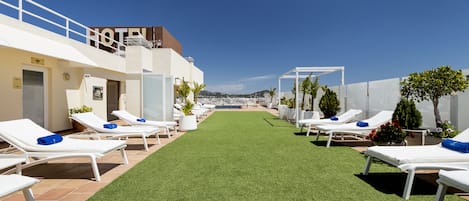 Een terras op het dak met witte ligbedden en een pad van kunstgras.