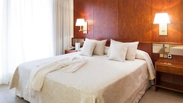 Habitación de hotel con una cama grande, cabecera de madera, dos mesitas de noche y un velador con una lámpara.