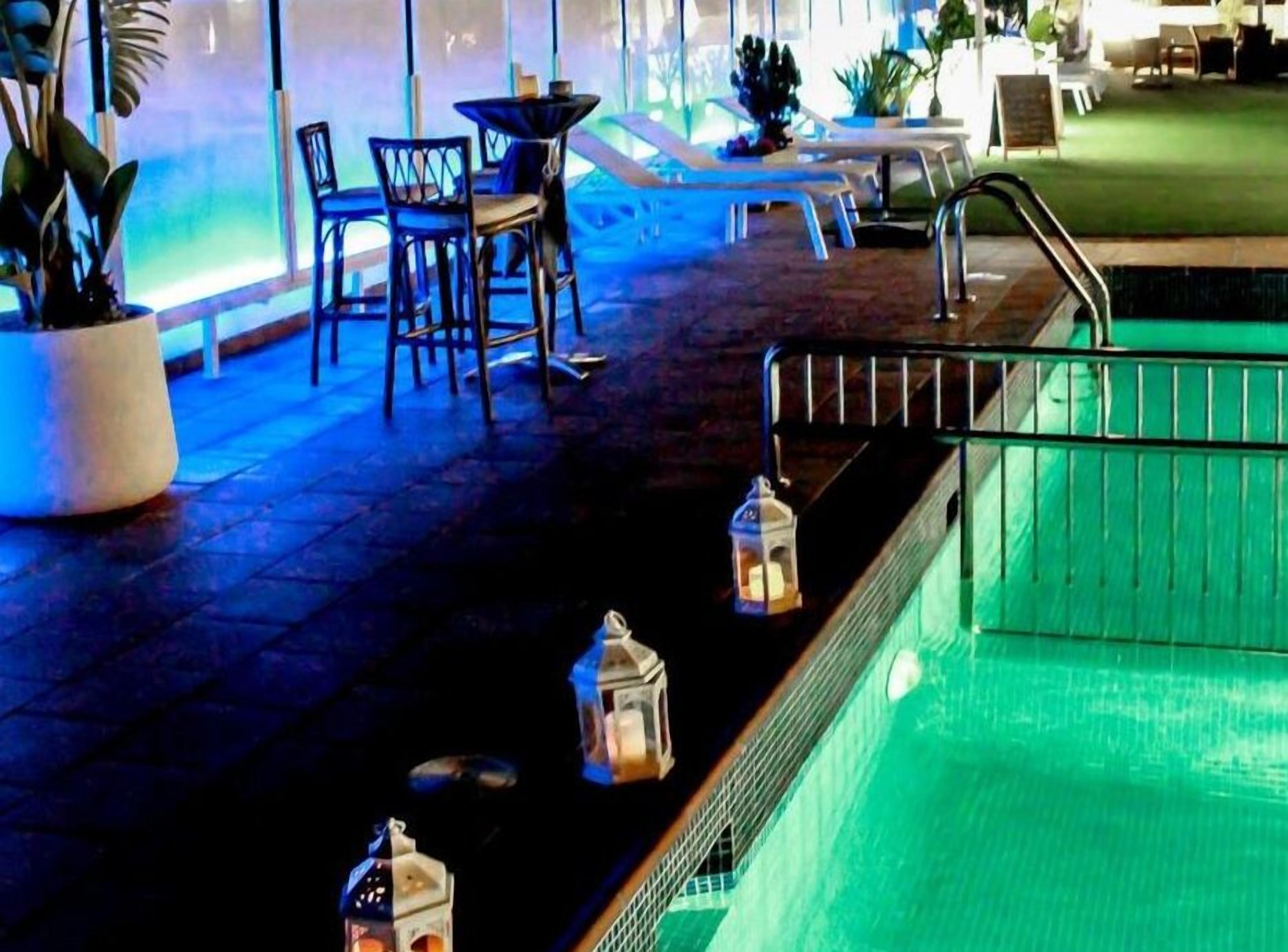 Un área junto a la piscina con sillas de descanso, una piscina pequeña y faroles decorativos.