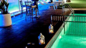 Un área junto a la piscina con sillas de descanso, una piscina pequeña y faroles decorativos.