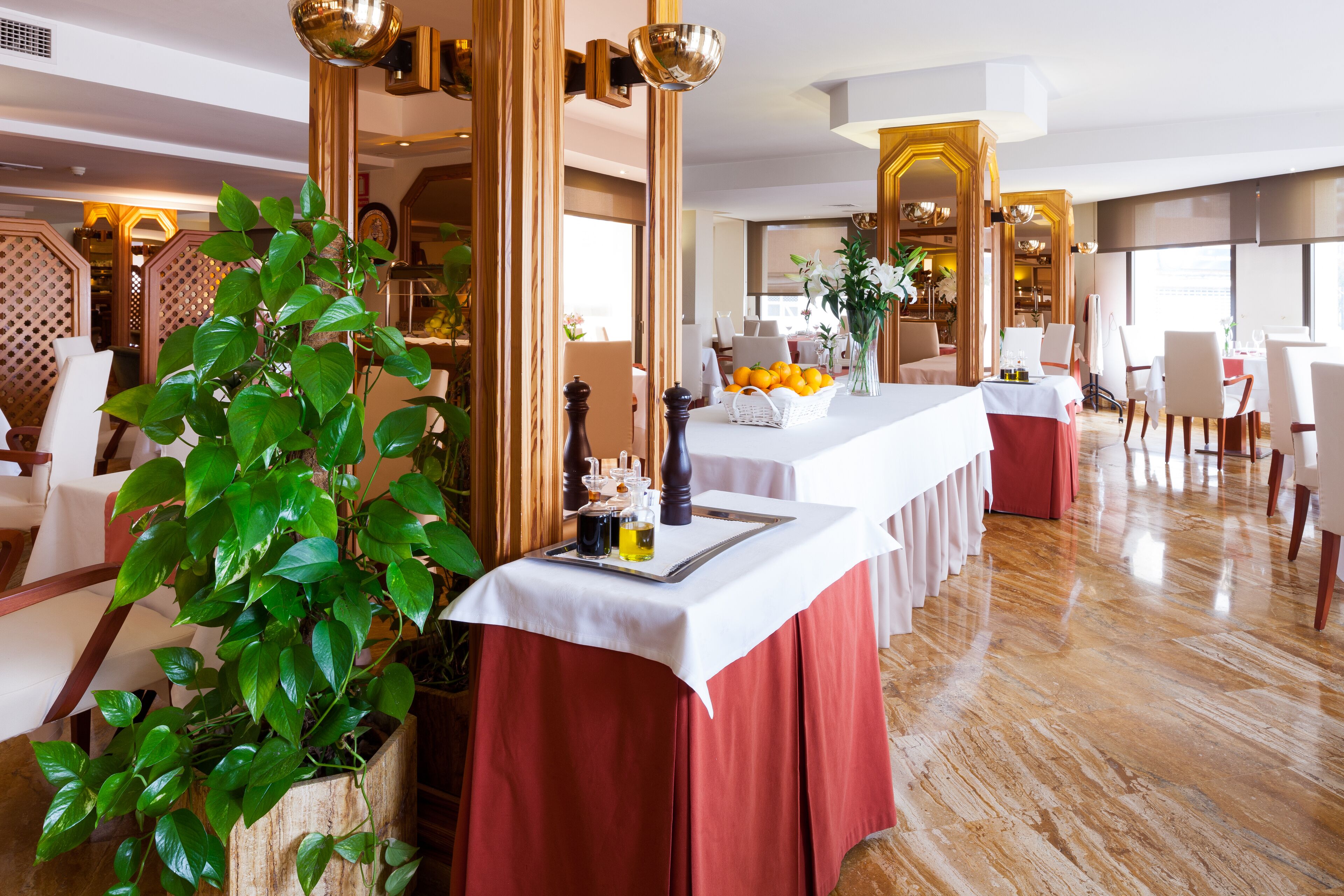 Un comedor de hotel con una mesa larga, cortinas rojas y una planta en maceta.