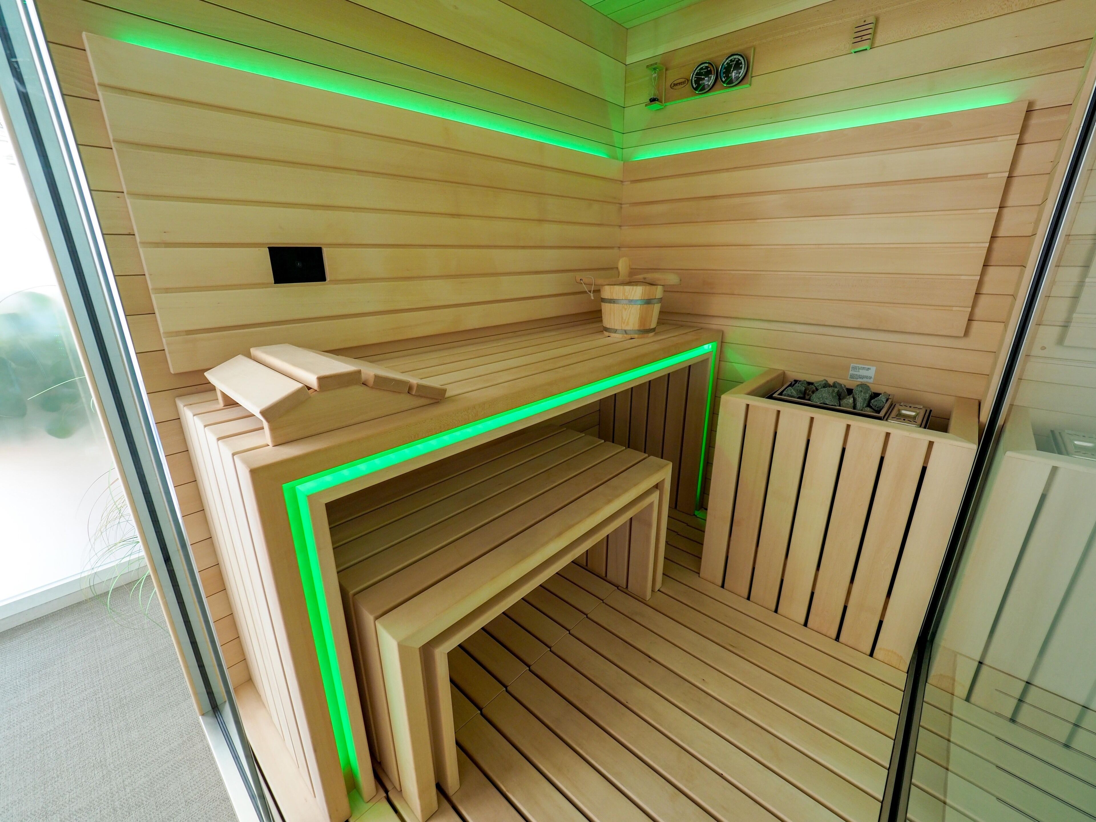 A sauna room with wooden slats, a bench, and a small wooden table with a bucket.
