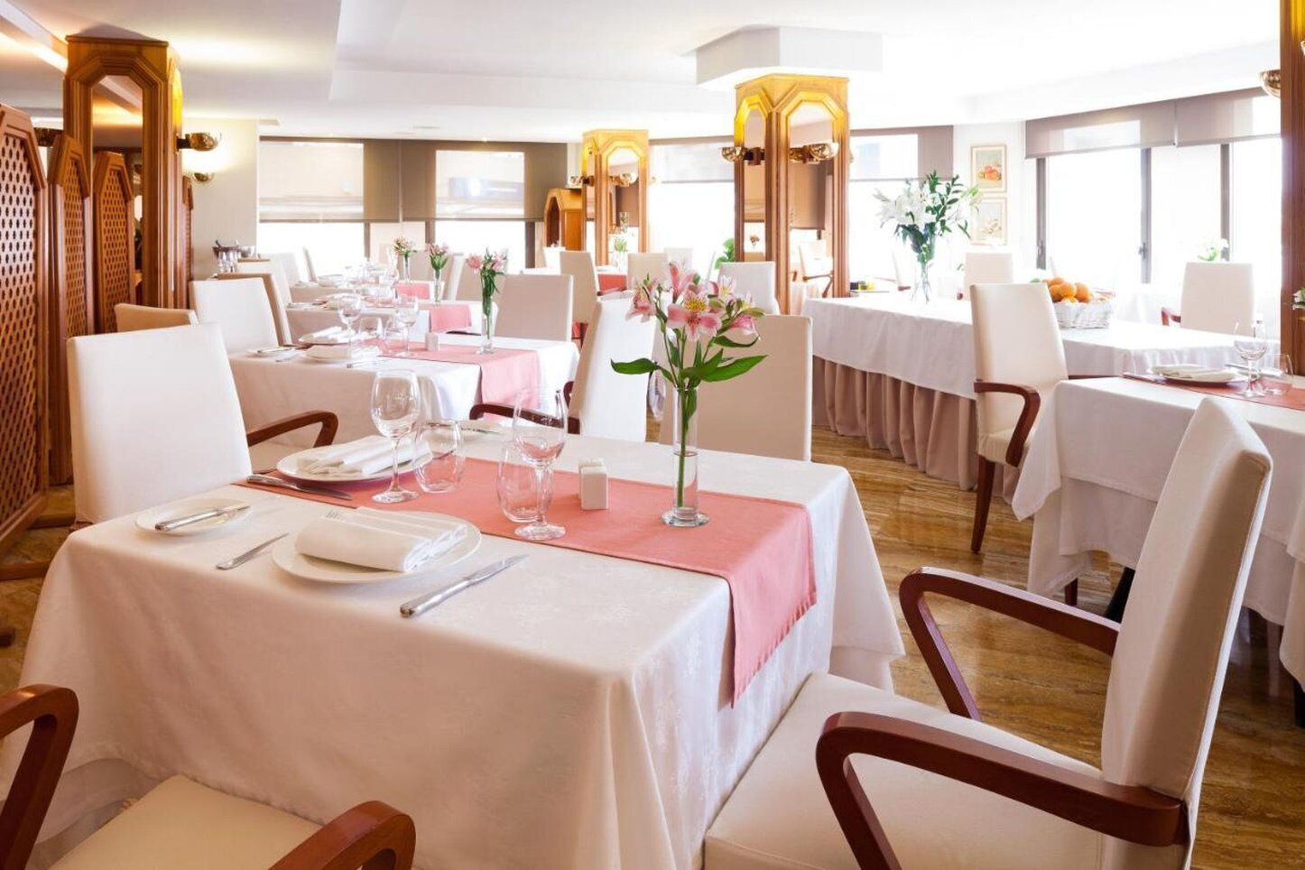 A well-lit dining area with tables set for service, featuring white tablecloths and pink placemats.