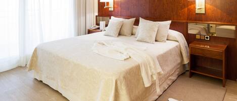 A neatly made bed with a patterned bedspread, two bedside lamps, a nightstand, and a mirror on the wall.