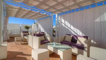 A covered outdoor seating area with wicker furniture and a glass table, featuring a clear view of the sky.