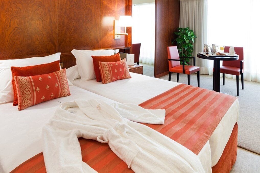 A hotel room with two beds, a sitting area with a table and chairs, and a large window.