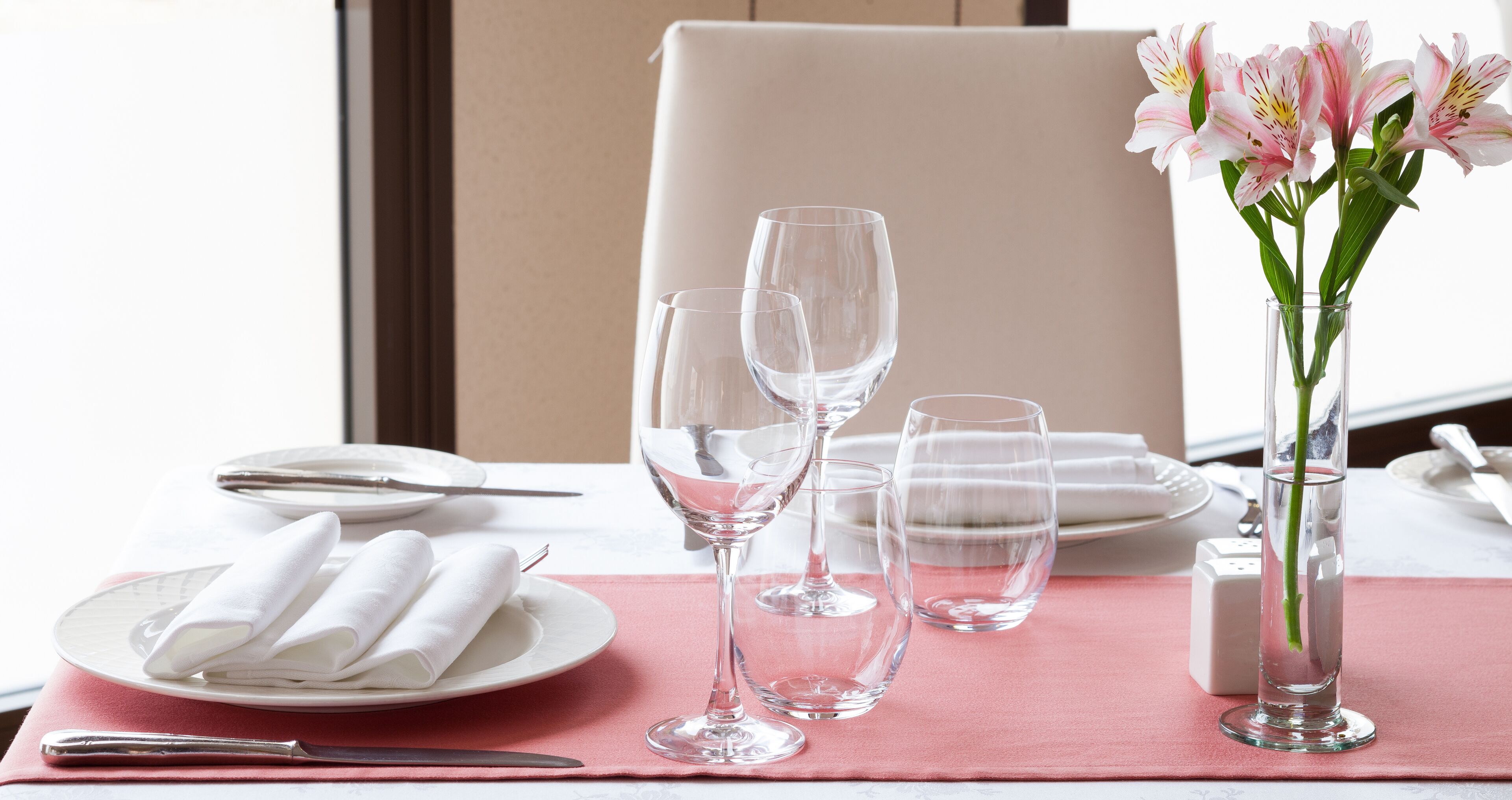 A dining table set with white plates, folded napkins, and clear wine glasses.