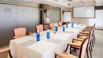 Un salón de conferencias con una larga mesa, sillas, una pantalla de proyector y paredes de vidrio con logotipos.