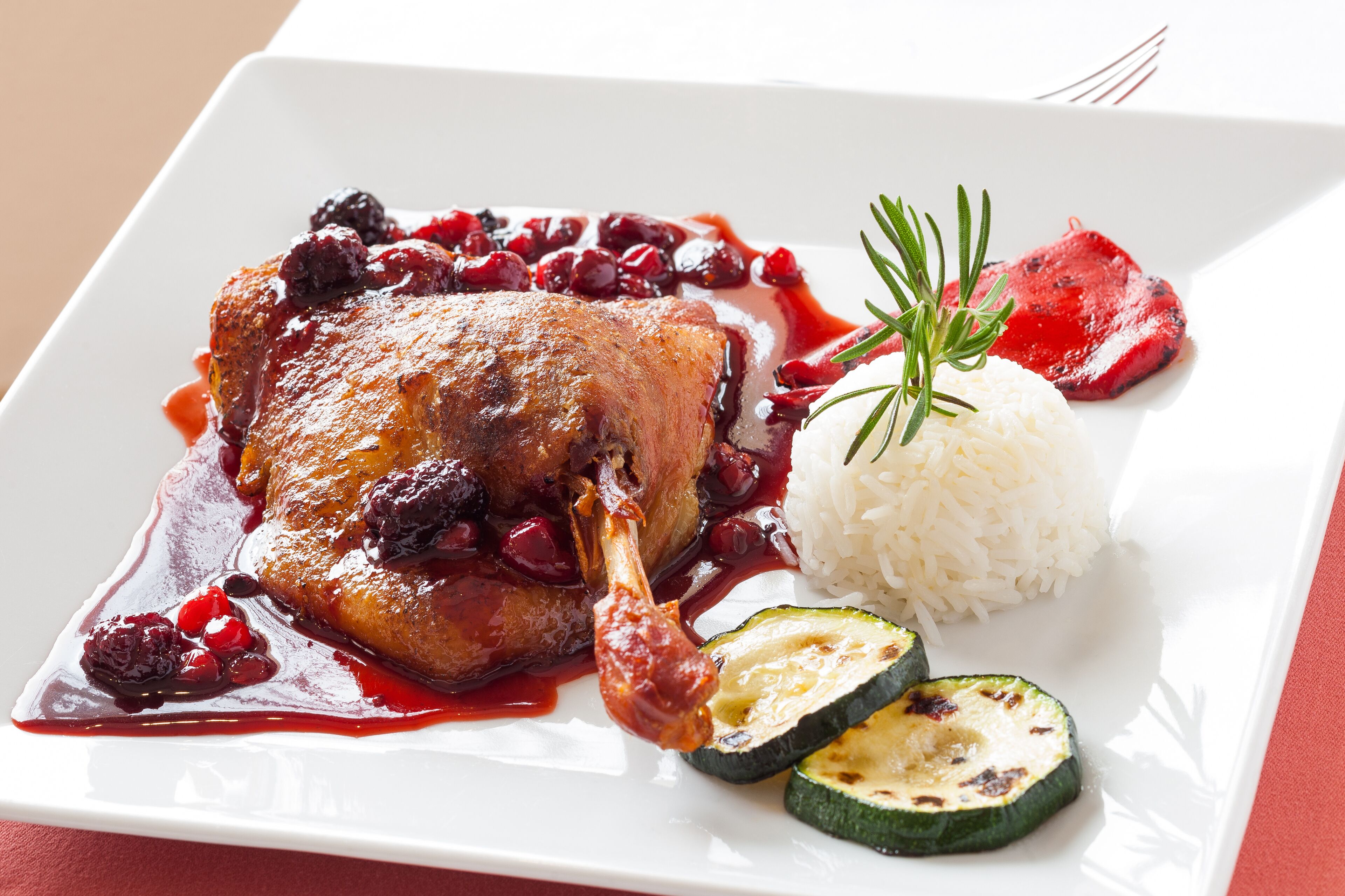 A plate with a roasted meat, cranberries, rice, and grilled zucchini.
