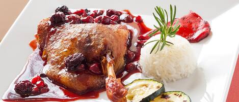 A plate with a roasted meat, cranberries, rice, and grilled zucchini.