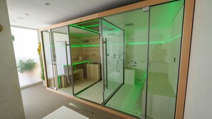 Una habitación moderna con paredes de vidrio, ducha, banco y una pequeña mesa, con iluminación ambiental verde.