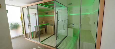 A modern, glass-walled room with a shower, a bench, and a small table, featuring green ambient lighting.