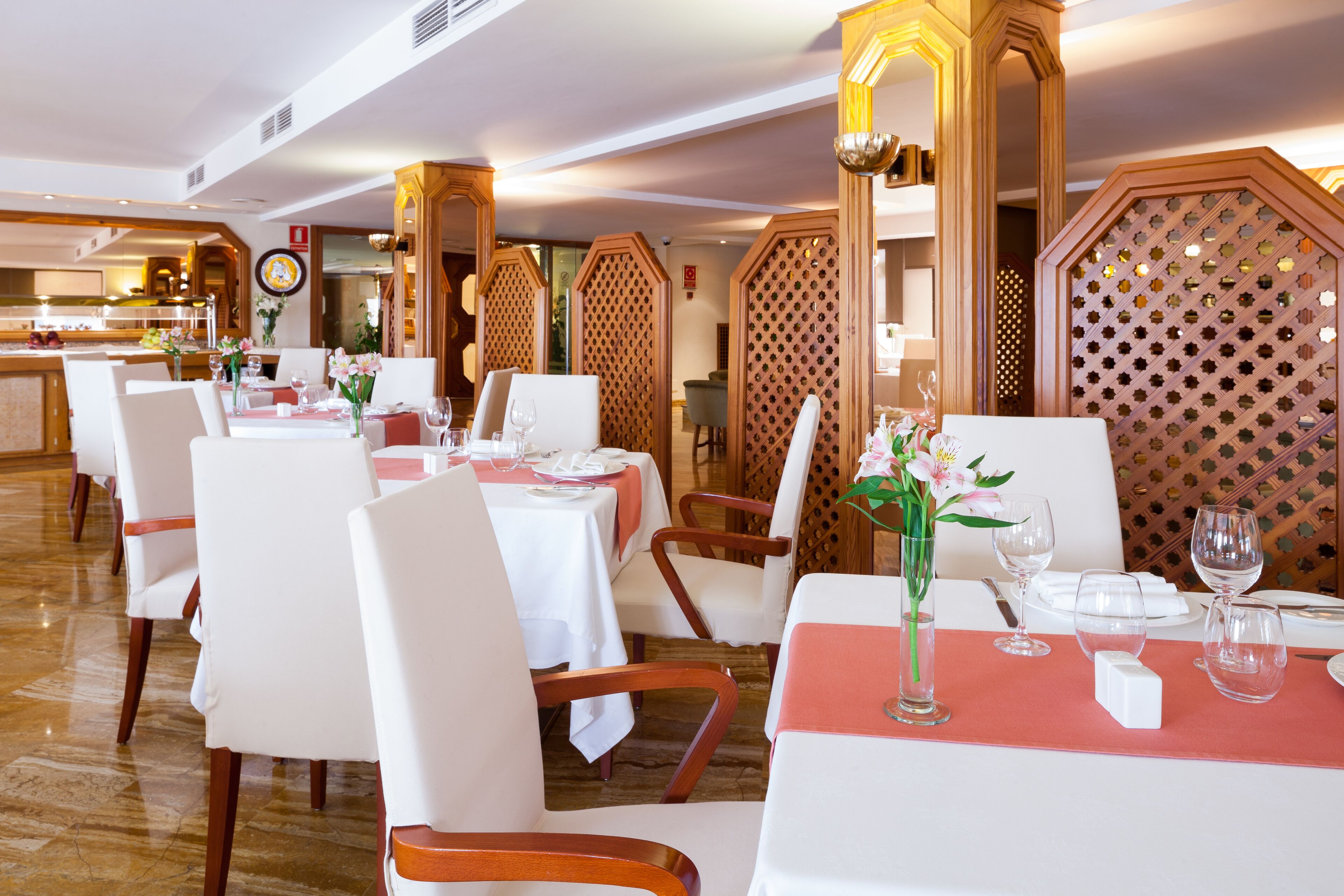 Un ristorante con tavoli e sedie bianche, tovaglie rosse e divisori in legno.