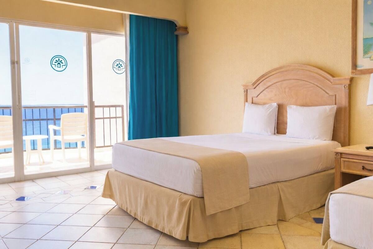 A hotel room with a bed, a nightstand, a chair, and a view of the sea through a sliding door.