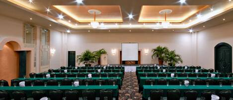 A conference room with rows of tables, chairs, and a projector screen at the front.