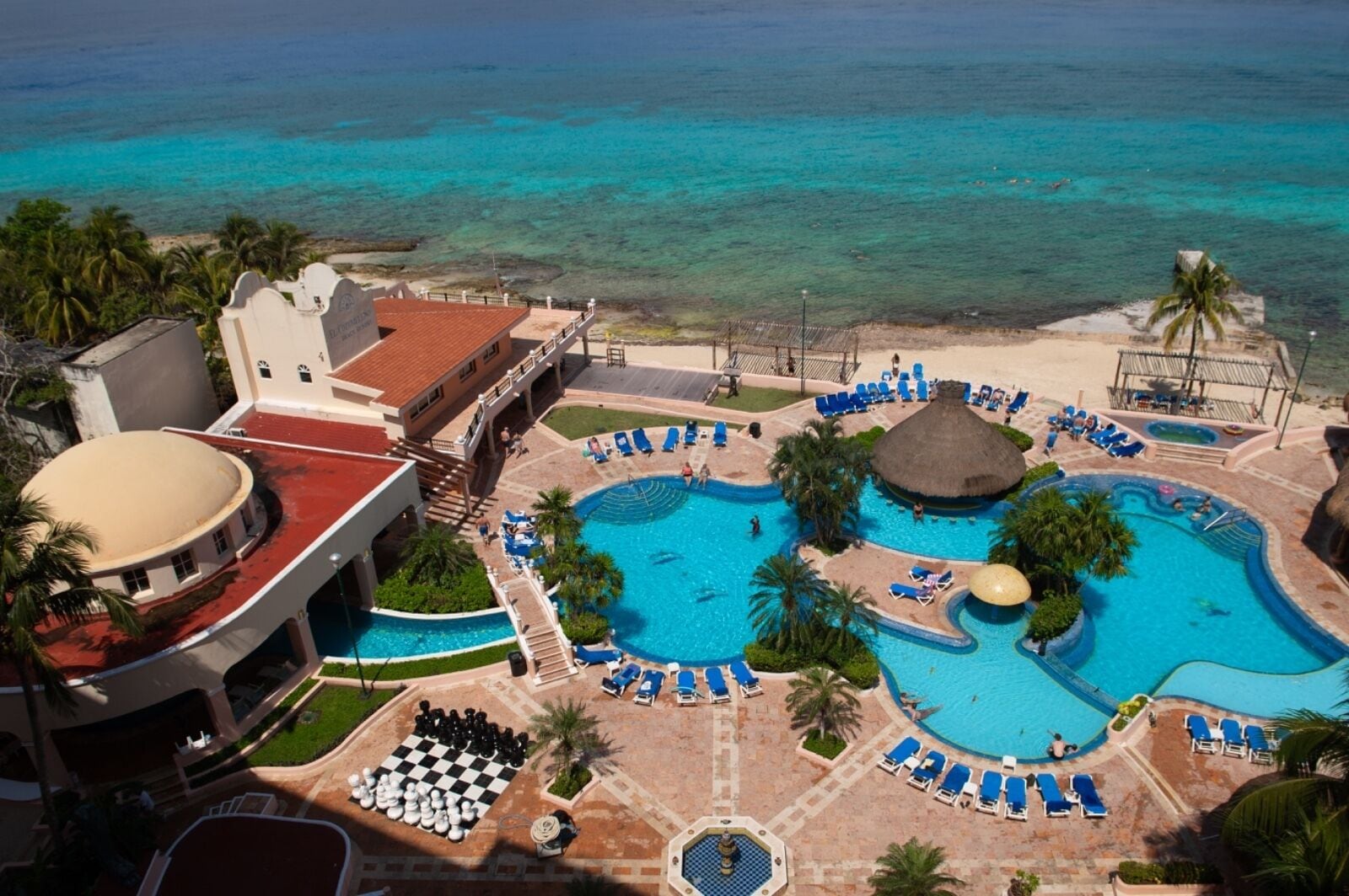 Un complexe hôtelier doté de plusieurs piscines, d’une plage et d’un grand bâtiment surmonté d’un toit rouge.