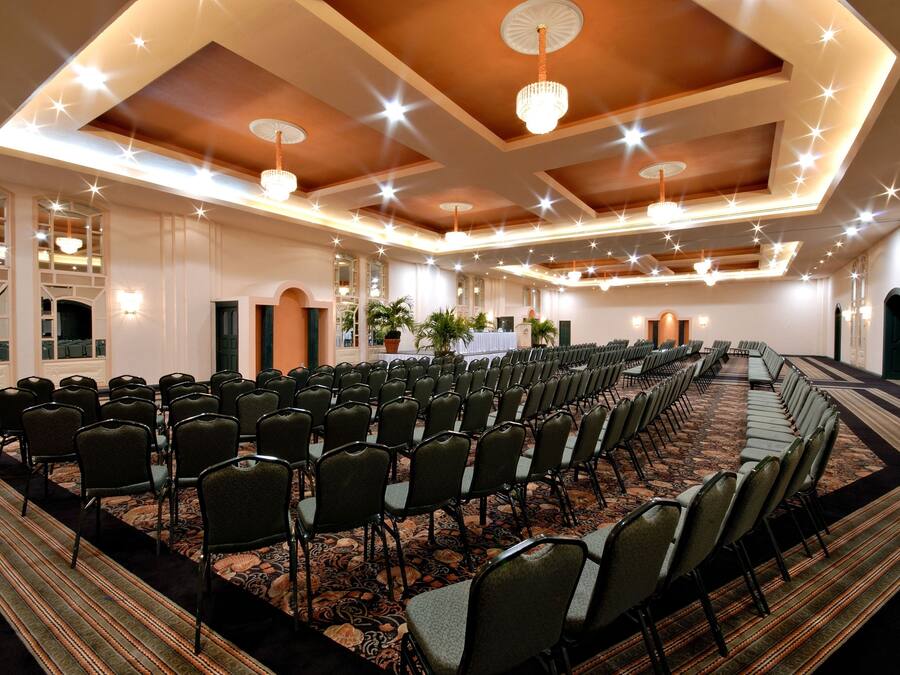 A conference room with rows of chairs, a patterned carpet, and chandeliers.
