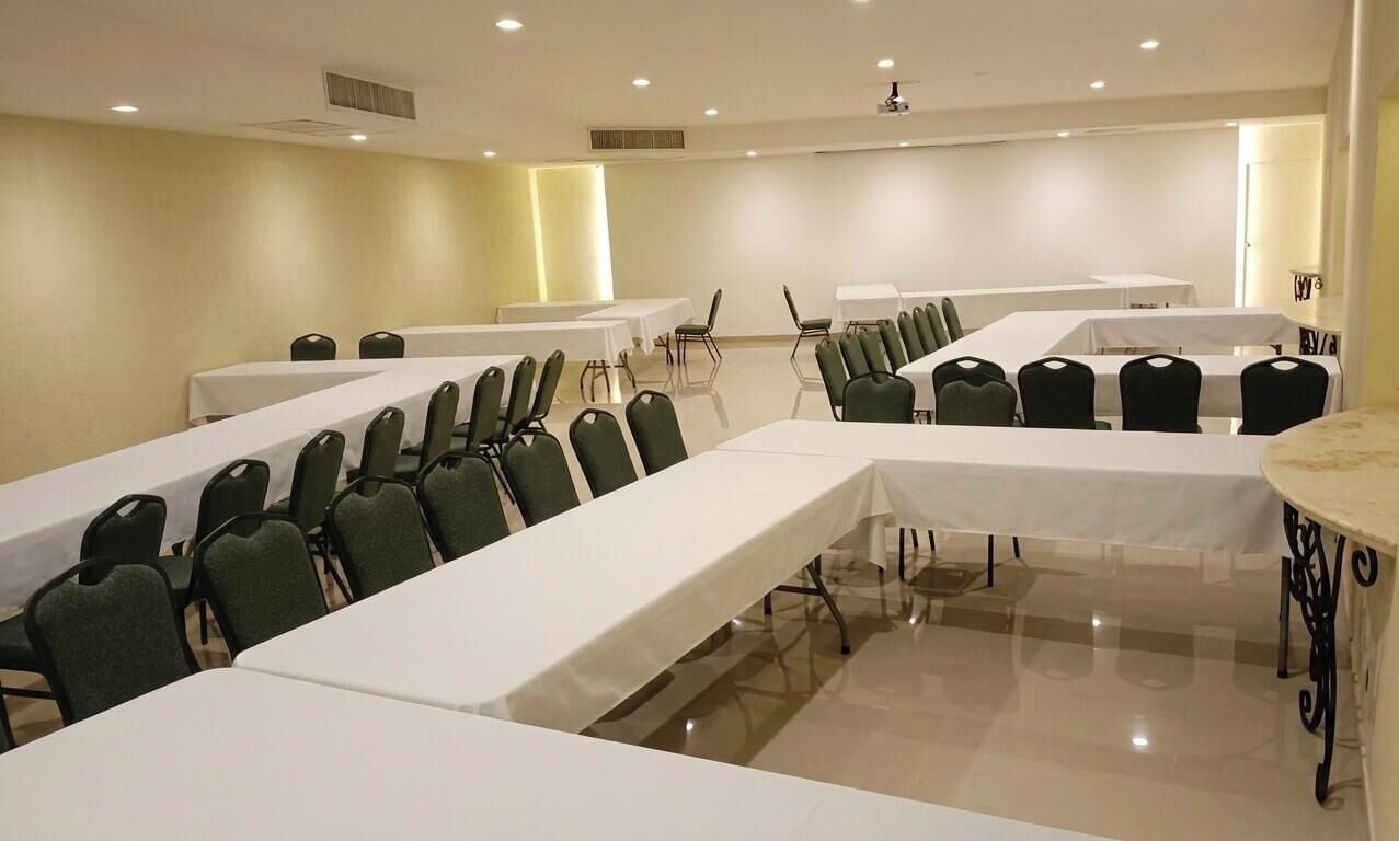 Une salle de conférence avec de longues tables et des chaises, un projecteur et un plafond blanc.