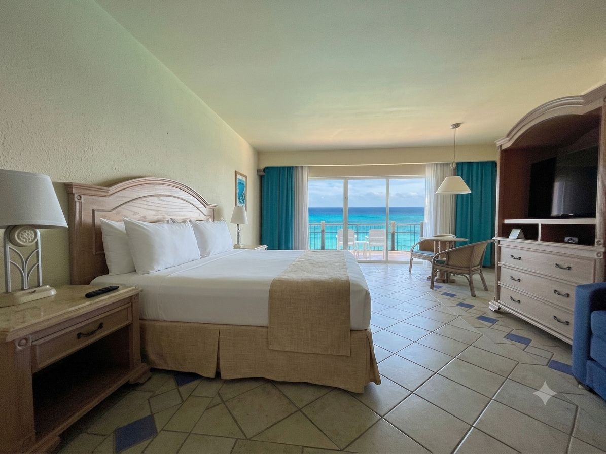 Habitación de hotel con cama, escritorio, silla, televisor y vista al océano.
