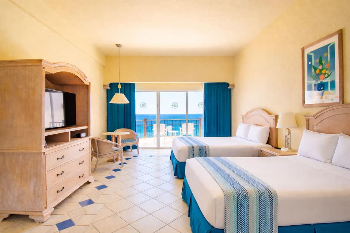 A hotel room with two beds, a TV, a dresser, a chair, and a balcony with a view.