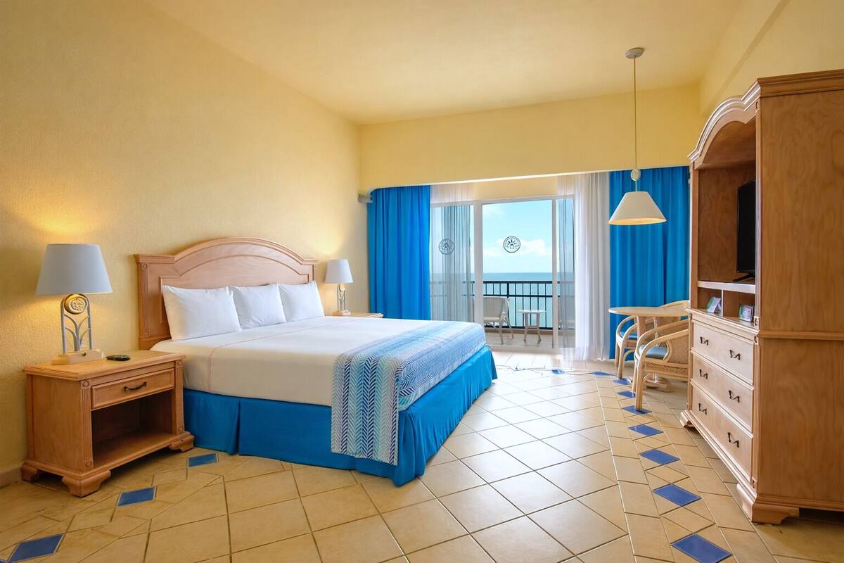 A hotel room with a bed, bedside tables, a wardrobe, a balcony with a view, and a tiled floor.