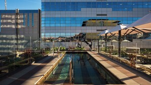 Un bâtiment moderne doté d’une façade en verre réfléchissant, d’une piscine et d’espaces de détente en plein air.