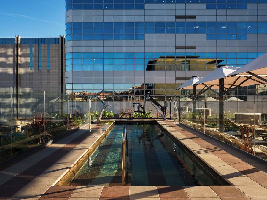 Un edificio moderno con fachada de vidrio reflectante, piscina y zonas de estar al aire libre.