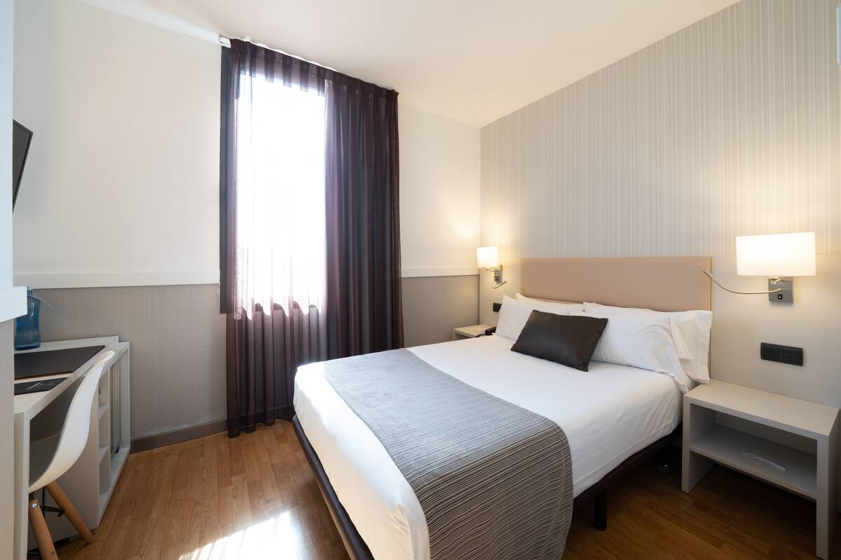 Een hotelkamer met een bed, nachtkastjes, een bureau en een raam met gordijnen.