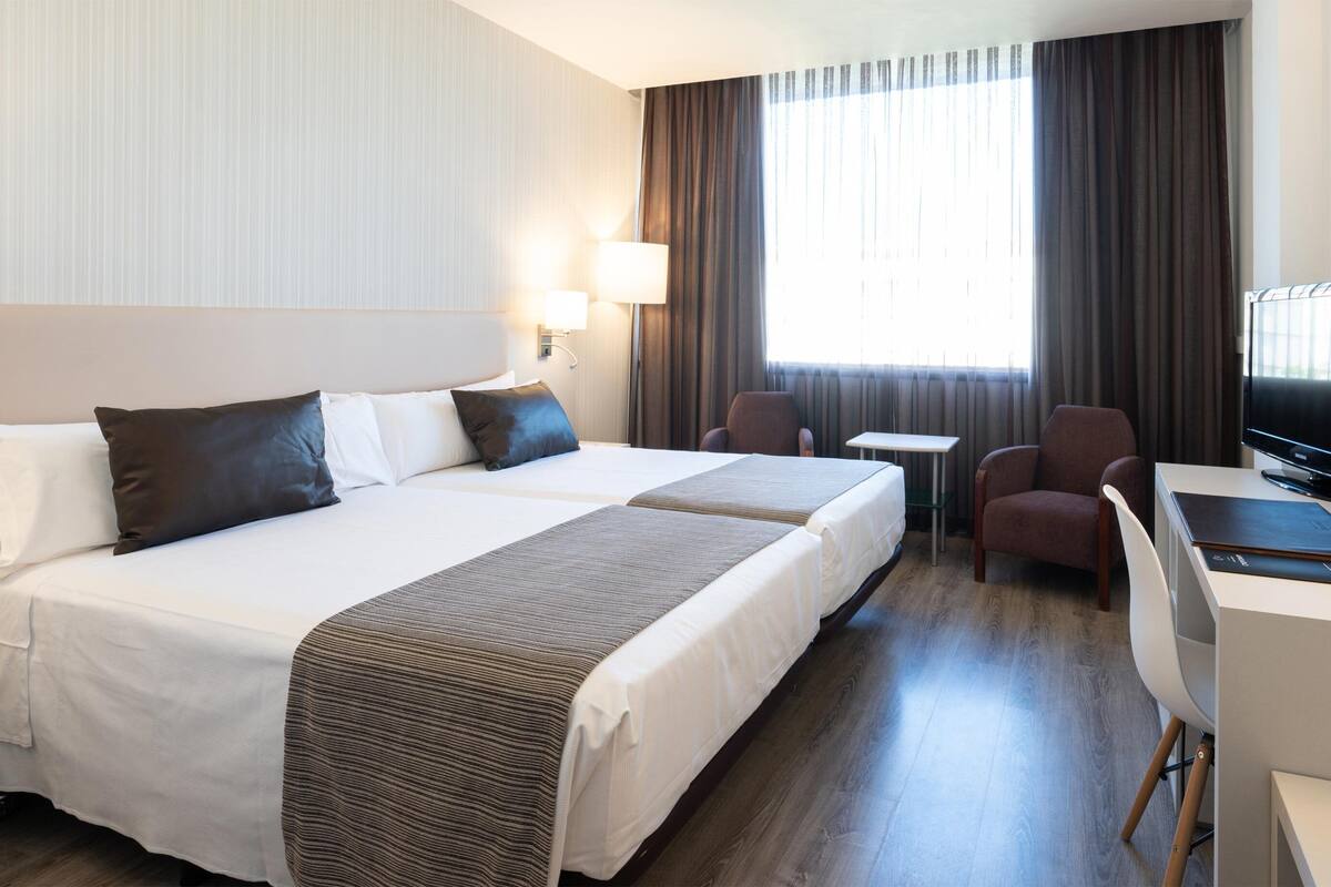 Een hotelkamer met twee bedden, een bureau, een stoel, een televisie en een raam met gordijnen.