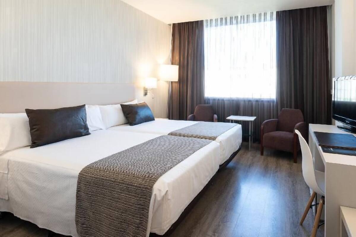 Een hotelkamer met twee bedden, een bureau, een stoel, een televisie en een raam met gordijnen.