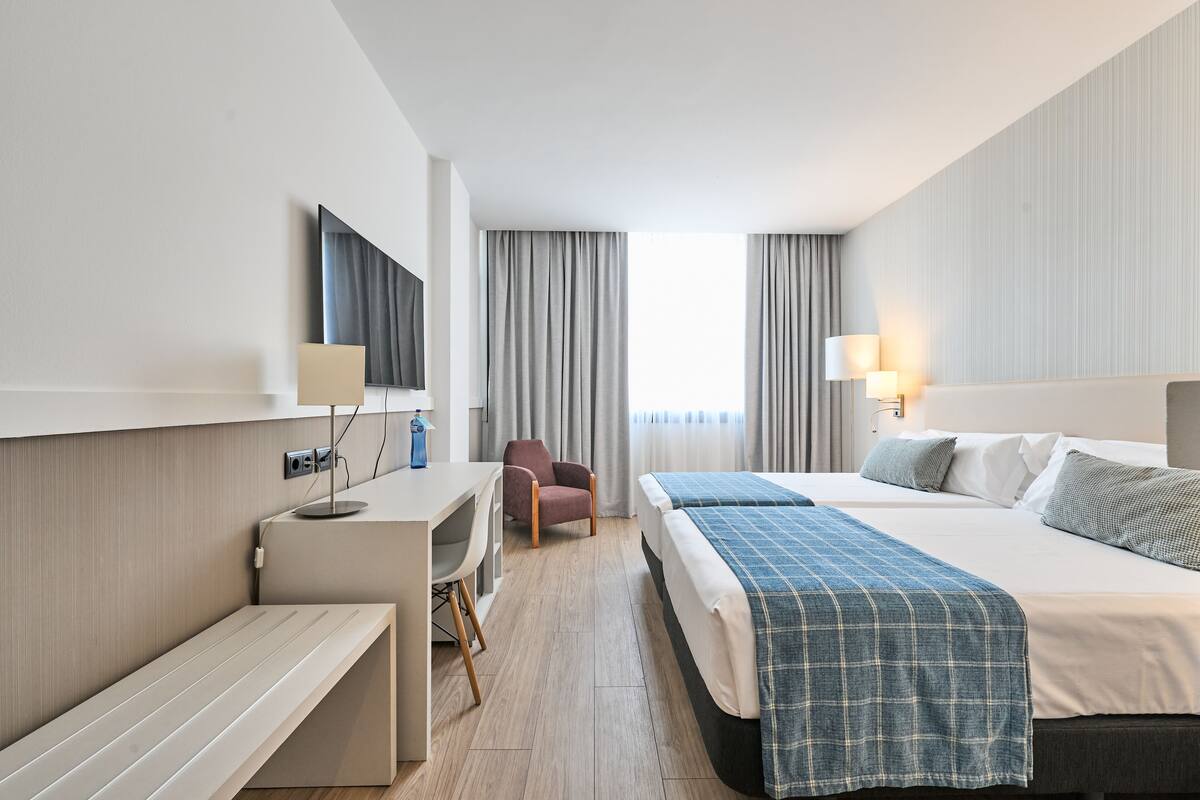 Een hotelkamer met een bed, bureau, stoel en een aan de muur bevestigde televisie.