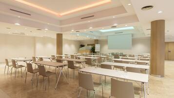 Un salón de conferencias con varias mesas y sillas, una pantalla grande y un atril.