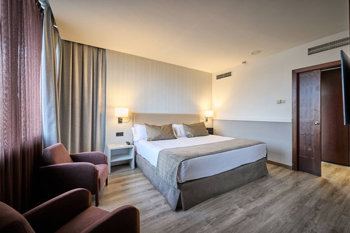 Een hotelkamer met een groot bed, twee nachtkastjes, een televisie en een zithoek met stoelen.