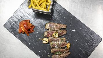Una pizarra de pizarra negra con carne en rodajas, ajo y un recipiente con papas fritas.