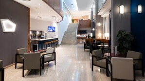 Un hall d’hôtel moderne doté d’un bar, de coins salon et d’un escalier menant aux étages supérieurs.
