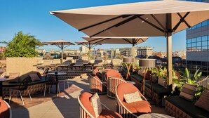 Un salon sur le toit, doté d’un espace extérieur avec des sièges, des parasols et une vue sur la ville.