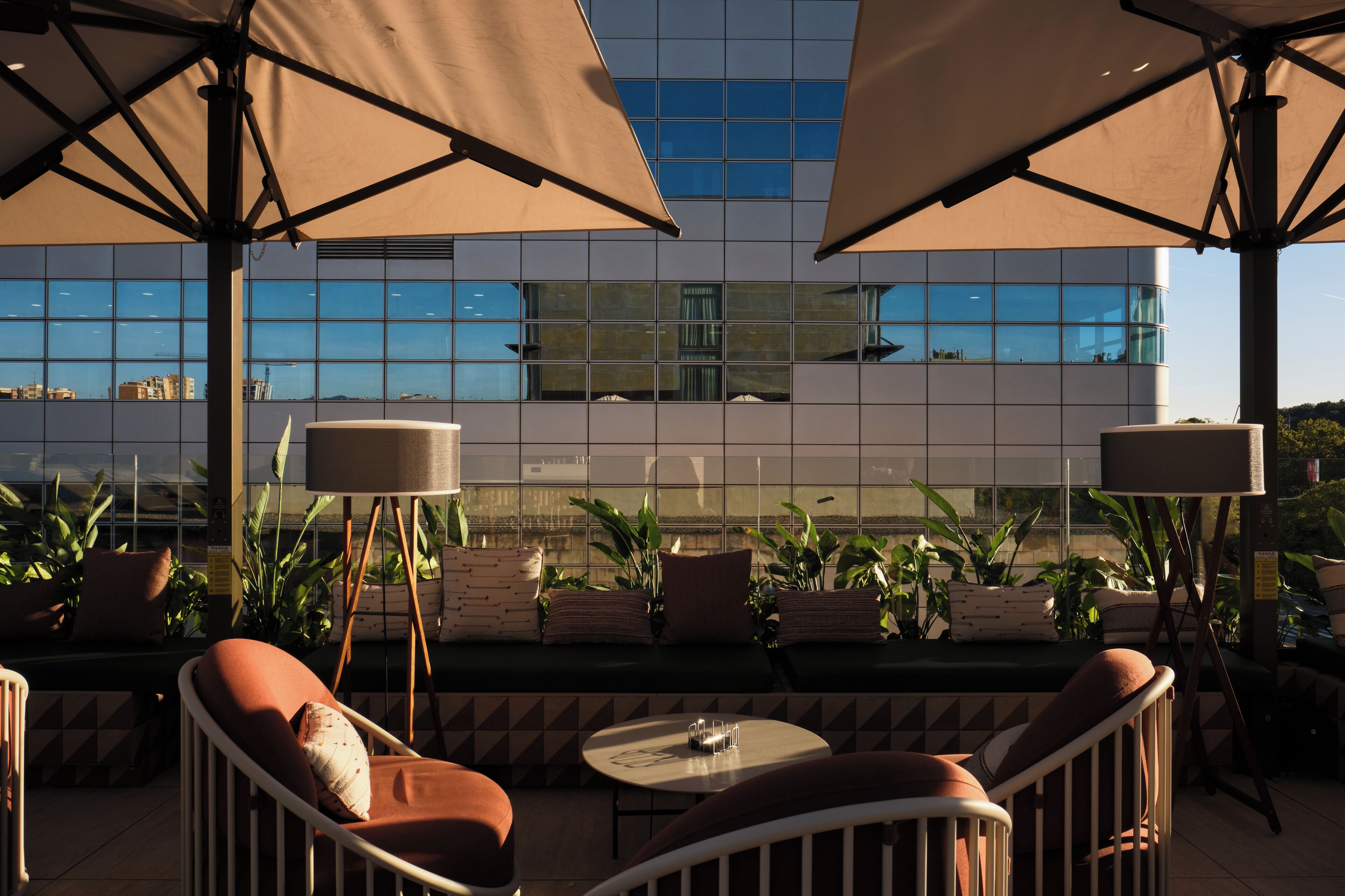 Una terraza en la azotea con mesas al aire libre, grandes sombrillas y vistas a un edificio moderno.