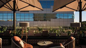 Una terraza en la azotea con mesas al aire libre, grandes sombrillas y vistas a un edificio moderno.