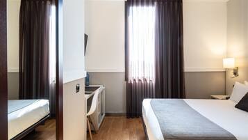 A hotel room with a bed, desk, and chair, a TV, and a window with curtains.